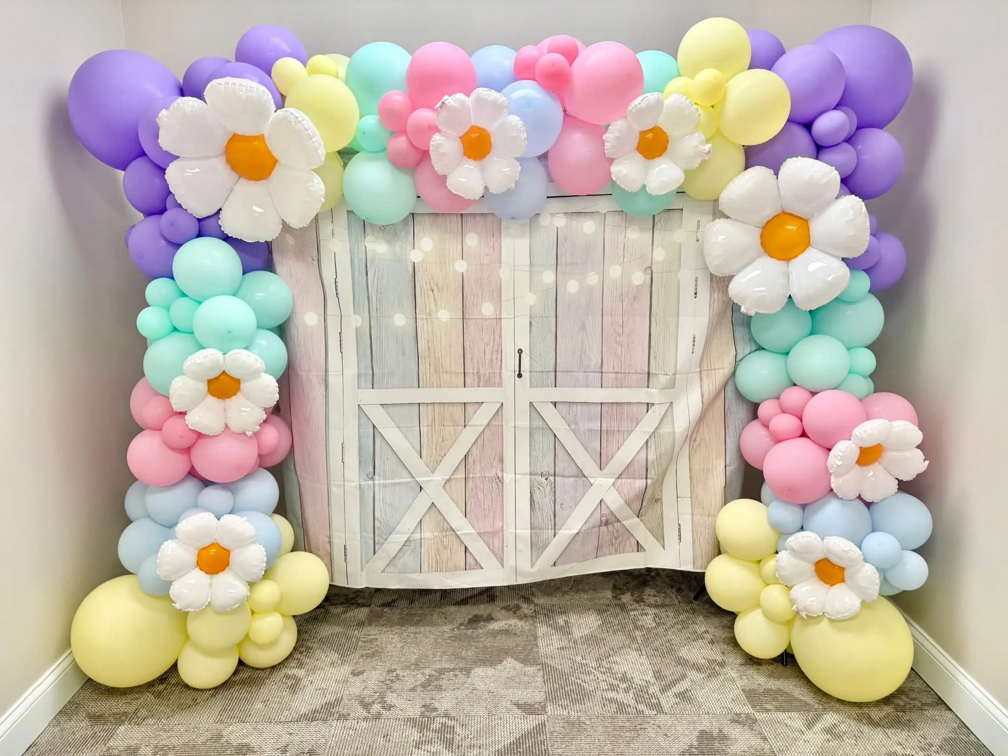 Pastel lavender, mint, pink, blue and yellow balloon garland with white daisy balloons around a barn-door backdrop