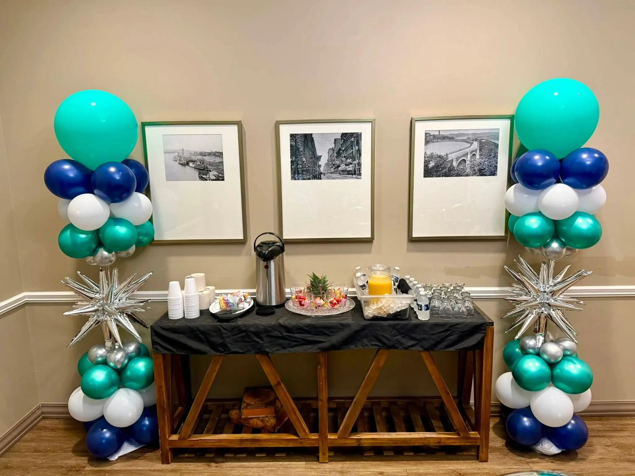 Two balloon columns in teal, navy, white and silver with silver starbursts, flanking a refreshment table