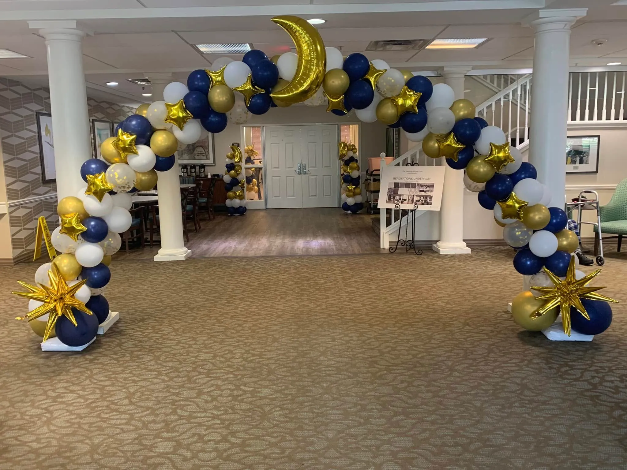 Walk-through arch of navy, white, gold and confetti balloons with a giant gold crescent moon, gold star foils and gold starbursts at the base