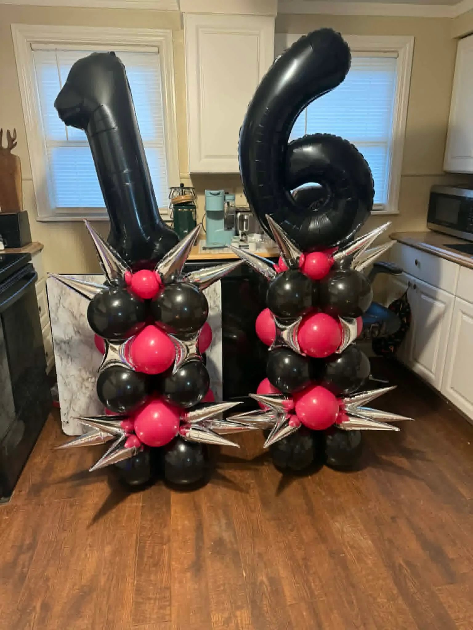 Two balloon columns of black and raspberry balloons with silver starbursts, topped with giant black 1 and 6 number balloons