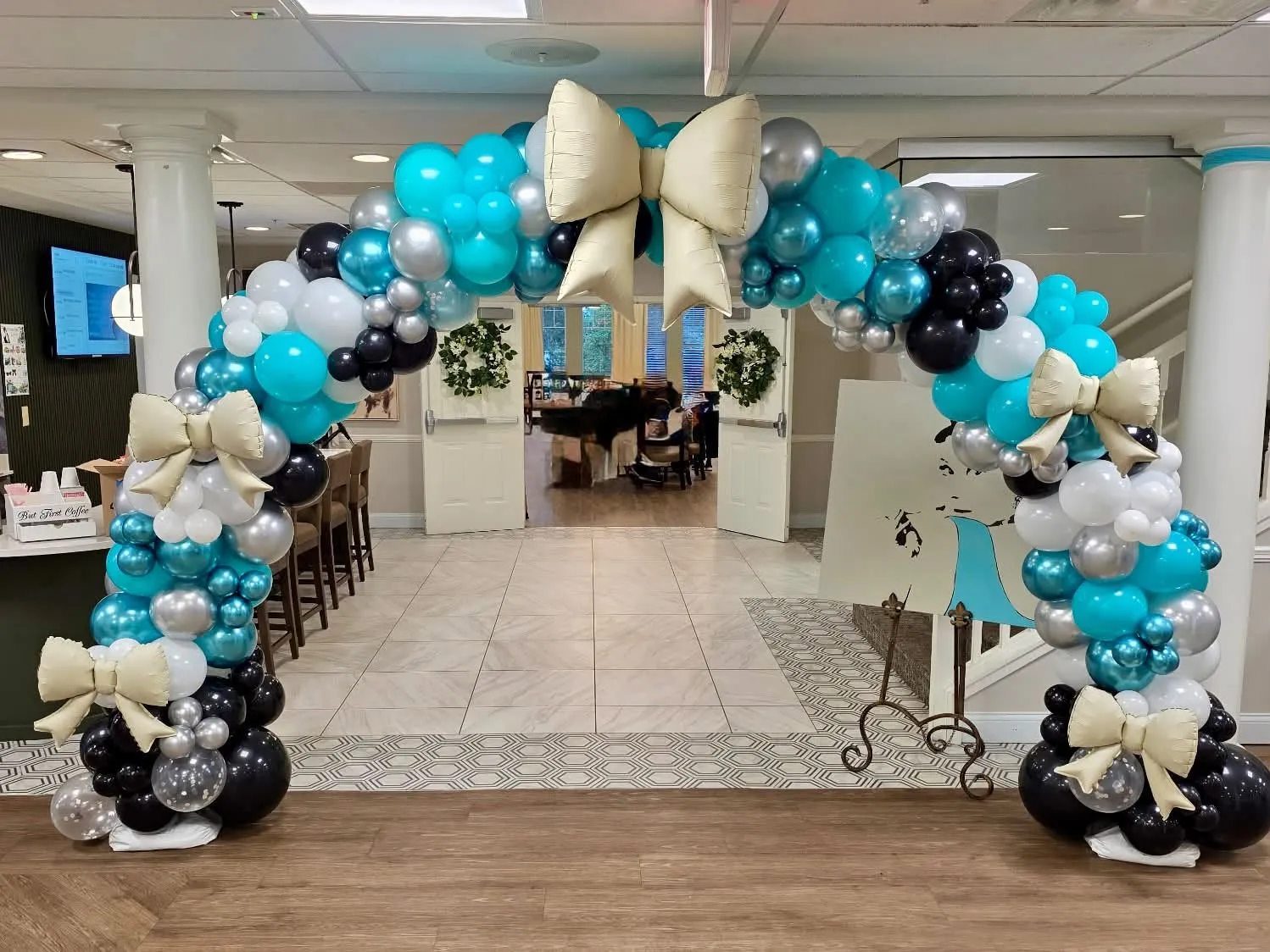 Full balloon arch in teal, chrome blue, silver, white and black with champagne-colored foil bows