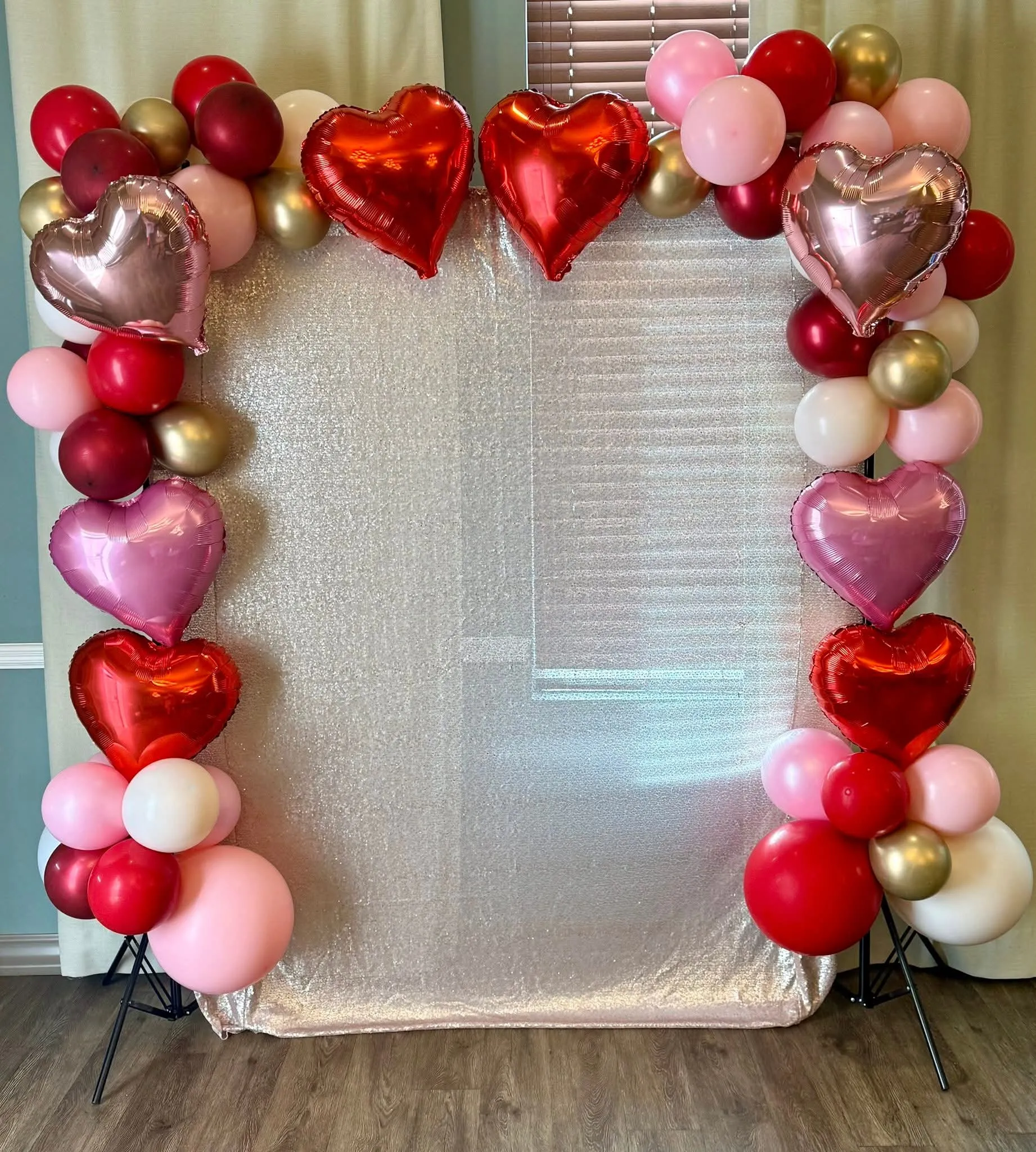 Red, pink, burgundy and gold balloon garland with heart foil balloons framing a shimmer backdrop